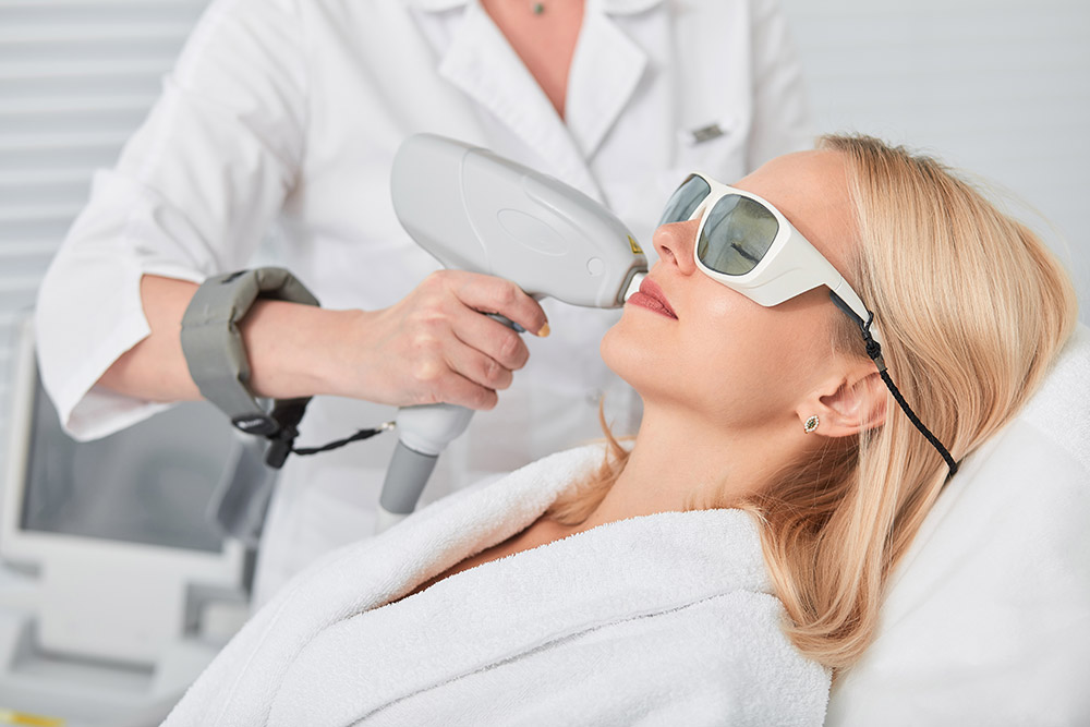 Eine junge Frau wird von Frau Dr. med. Annette Müller mit einem Laser im Gesicht behandelt.